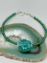 Load image into Gallery viewer, This blue-green pressed glass floral beaded bracelet is a nature-inspired accessory that adds a hint of summer to any look. Crafted with intricate green-blue pressed glass beads and metal wire, the bracelet has an iridescent shimmer finish and a lobster claw clasp for secure wear. Perfect for day-to-night looks.  Measurements:  Bracelet: 8 1/2" in length