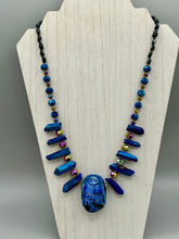 Load image into Gallery viewer, Powerful statement piece necklace features an eye-catching hand sculpted dark blue clay scarab beetle pendant. Adorned with vibrant sapphire luster quartz nuggets and sapphire faceted glass beaded necklace, this dramatic necklace artfully wraps around the neck, conveying an elegant and bold style. The Egyptian scarab symbol of rebirth, regeneration, and protection in the afterlife. Secure toggle clasp - Necklace is 23" length