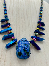 Load image into Gallery viewer, Powerful statement piece necklace features an eye-catching hand sculpted dark blue clay scarab beetle pendant. Adorned with vibrant sapphire luster quartz nuggets and sapphire faceted glass beaded necklace, this dramatic necklace artfully wraps around the neck, conveying an elegant and bold style. The Egyptian scarab symbol of rebirth, regeneration, and protection in the afterlife. Secure toggle clasp - Necklace is 23" length