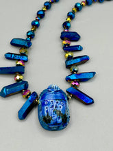 Load image into Gallery viewer, Powerful statement piece necklace features an eye-catching hand sculpted dark blue clay scarab beetle pendant. Adorned with vibrant sapphire luster quartz nuggets and sapphire faceted glass beaded necklace, this dramatic necklace artfully wraps around the neck, conveying an elegant and bold style. The Egyptian scarab symbol of rebirth, regeneration, and protection in the afterlife. Secure toggle clasp - Necklace is 23" length