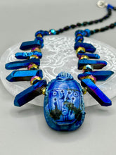 Load image into Gallery viewer, Powerful statement piece necklace features an eye-catching hand sculpted dark blue clay scarab beetle pendant. Adorned with vibrant sapphire luster quartz nuggets and sapphire faceted glass beaded necklace, this dramatic necklace artfully wraps around the neck, conveying an elegant and bold style. The Egyptian scarab symbol of rebirth, regeneration, and protection in the afterlife. Secure toggle clasp - Necklace is 23" length