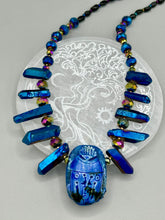 Load image into Gallery viewer, Powerful statement piece necklace features an eye-catching hand sculpted dark blue clay scarab beetle pendant. Adorned with vibrant sapphire luster quartz nuggets and sapphire faceted glass beaded necklace, this dramatic necklace artfully wraps around the neck, conveying an elegant and bold style. The Egyptian scarab symbol of rebirth, regeneration, and protection in the afterlife. Secure toggle clasp - Necklace is 23" length