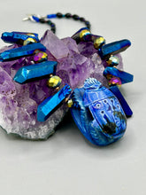 Load image into Gallery viewer, Powerful statement piece necklace features an eye-catching hand sculpted dark blue clay scarab beetle pendant. Adorned with vibrant sapphire luster quartz nuggets and sapphire faceted glass beaded necklace, this dramatic necklace artfully wraps around the neck, conveying an elegant and bold style. The Egyptian scarab symbol of rebirth, regeneration, and protection in the afterlife. Secure toggle clasp - Necklace is 23" length