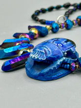 Load image into Gallery viewer, Powerful statement piece necklace features an eye-catching hand sculpted dark blue clay scarab beetle pendant. Adorned with vibrant sapphire luster quartz nuggets and sapphire faceted glass beaded necklace, this dramatic necklace artfully wraps around the neck, conveying an elegant and bold style. The Egyptian scarab symbol of rebirth, regeneration, and protection in the afterlife. Secure toggle clasp - Necklace is 23" length