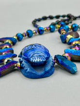 Load image into Gallery viewer, Powerful statement piece necklace features an eye-catching hand sculpted dark blue clay scarab beetle pendant. Adorned with vibrant sapphire luster quartz nuggets and sapphire faceted glass beaded necklace, this dramatic necklace artfully wraps around the neck, conveying an elegant and bold style. The Egyptian scarab symbol of rebirth, regeneration, and protection in the afterlife. Secure toggle clasp - Necklace is 23" length
