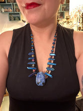 Load image into Gallery viewer, Powerful statement piece necklace features an eye-catching hand sculpted dark blue clay scarab beetle pendant. Adorned with vibrant sapphire luster quartz nuggets and sapphire faceted glass beaded necklace, this dramatic necklace artfully wraps around the neck, conveying an elegant and bold style. The Egyptian scarab symbol of rebirth, regeneration, and protection in the afterlife. Secure toggle clasp - Necklace is 23" length