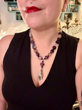 Load image into Gallery viewer, This nature-inspired accessory features an array of unique hues, including rainbow fluorite stone beads and iridescent dark shimmery purple glass beads with hints of gold, blue, pink, and green. The secure hook-eye clasp makes it perfect for day to night wear, allowing you to add a touch of summer to your wardrobe. The necklace is further complemented by a large square-shaped rainbow fluorite bead and a lucky hand charm. Measurements: Necklace: 18", Lucky hand pendant 3"