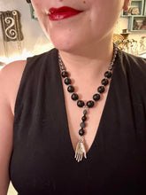 Load image into Gallery viewer, This elegant hematite and black glass beaded necklace is the perfect accessory for your unique look. With a large black and gray glass beads adorned with a lucky hand charm, it exudes a dark, alluring vibe. Complemented with floral shaped metal beads, it will make a bold statement. Measurements: Necklace: 18” in length - lucky hand charm is 3 1 /2” Height