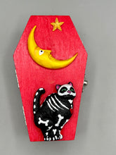 Load image into Gallery viewer, Coffin keepsake box represents the eternal love for a special kitty cat in your life. Cat silhouette sitting admiring the moon and stars. Day Of The Dead art was created for the cat lovers who adore their sweet kitty. Coffin-shaped box features a bright and vibrant red exterior, with an adoring yellow crescent moon and star. Complemented with a shimmery blue ribbon and smiling moon, the inside is painted in a bright bluer hue with black floral cross and detailing a traditional Mexican-themed fabric.