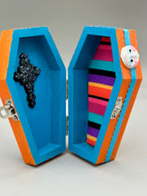Load image into Gallery viewer, Coffin keepsake box represents the eternal love for a special kitty cat in your life. Cat silhouette sitting admiring the moon and stars. Day Of The Dead art was created for the cat lovers who adore their sweet kitty. Coffin-shaped box features a bright and vibrant orange exterior, with an adoring blue crescent moon and yellow star. Complemented with a shimmery blue ribbon and smiling moon, the inside is painted in a bright blue hue with black floral cross and detailing a traditional Mexican-themed fabric.