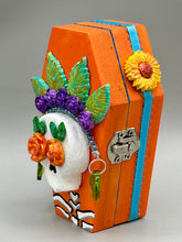 Load image into Gallery viewer, This coffin-shaped box features a bright and colorful exterior, showcasing a vibrant Frida Kahlo inspired calavera.  This beautifully handcrafted calavera is adorned with  Frida's iconic floral crown. To complete the look, the inside is also painted in colorful hues with a black and silver floral cross. The interior is also finished with a traditional Mexican-themed fabric.  L: 4 1/2“; W: 2 ½”; H: 1 5/8”