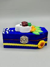 Load image into Gallery viewer, This coffin-shaped box features a bright and colorful exterior, showcasing a vibrant Frida Kahlo inspired calavera.  This beautifully handcrafted calavera is adorned with  Frida's iconic floral crown. To complete the look, the inside is also painted in colorful hues with a black and silver floral cross. The interior is also finished with a traditional Mexican-themed fabric.  L: 4 1/2“; W: 2 ½”; H: 1 5/8”