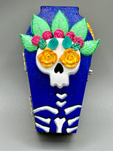 Load image into Gallery viewer, This coffin-shaped box features a bright and colorful exterior, showcasing a vibrant Frida Kahlo inspired calavera. This beautifully handcrafted calavera is adorned with Frida's iconic floral crown. To complete the look, the inside is also painted in colorful hues with a black and silver floral cross. The interior is also finished with a traditional Mexican-themed fabric. L: 4 1/2“; W: 2 ½”; H: 1 5/8”