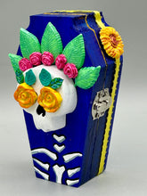 Load image into Gallery viewer, This coffin-shaped box features a bright and colorful exterior, showcasing a vibrant Frida Kahlo inspired calavera. This beautifully handcrafted calavera is adorned with Frida's iconic floral crown. To complete the look, the inside is also painted in colorful hues with a black and silver floral cross. The interior is also finished with a traditional Mexican-themed fabric. L: 4 1/2“; W: 2 ½”; H: 1 5/8”