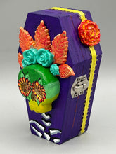 Load image into Gallery viewer, This coffin-shaped box features a bright and colorful exterior, showcasing a vibrant Frida Kahlo inspired calavera.  This beautifully handcrafted calavera is adorned with  Frida's iconic floral crown. To complete the look, the inside is also painted in colorful hues with a black and silver floral cross. The interior is also finished with a traditional Mexican-themed fabric.  L: 4 1/2“; W: 2 ½”; H: 1 5/8”