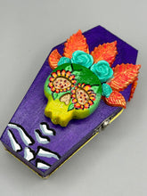Load image into Gallery viewer, This coffin-shaped box features a bright and colorful exterior, showcasing a vibrant Frida Kahlo inspired calavera.  This beautifully handcrafted calavera is adorned with  Frida's iconic floral crown. To complete the look, the inside is also painted in colorful hues with a black and silver floral cross. The interior is also finished with a traditional Mexican-themed fabric.  L: 4 1/2“; W: 2 ½”; H: 1 5/8”