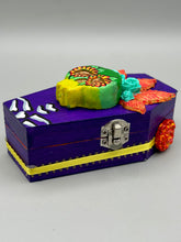 Load image into Gallery viewer, This coffin-shaped box features a bright and colorful exterior, showcasing a vibrant Frida Kahlo inspired calavera.  This beautifully handcrafted calavera is adorned with  Frida's iconic floral crown. To complete the look, the inside is also painted in colorful hues with a black and silver floral cross. The interior is also finished with a traditional Mexican-themed fabric.  L: 4 1/2“; W: 2 ½”; H: 1 5/8”