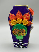 Load image into Gallery viewer, This coffin-shaped box features a bright and colorful exterior, showcasing a vibrant Frida Kahlo inspired calavera.  This beautifully handcrafted calavera is adorned with  Frida's iconic floral crown. To complete the look, the inside is also painted in colorful hues with a black and silver floral cross. The interior is also finished with a traditional Mexican-themed fabric.  L: 4 1/2“; W: 2 ½”; H: 1 5/8”