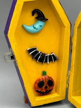 Load image into Gallery viewer, Coffin shaped box features a Day of the Dead kitty cat wearing a cute witchy hat while standing next to her witchy broom and a flying bat friend. The inside of the coffin is adorned with a witchy crescent moon, Jack-O-Lantern and a cute bat. This captivating coffin box makes an eye-catching, bewitching and whimsical Halloween-themed art piece that adds a one-of-a-kind Halloween touch to any home or office. L: 4 7/8"; W: 3"; H: 1 1/2"