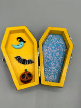 Load image into Gallery viewer, Coffin shaped box features a Day of the Dead kitty cat wearing a cute witchy hat while standing next to her witchy broom and a flying bat friend. The inside of the coffin is adorned with a witchy crescent moon, Jack-O-Lantern and a cute bat. This captivating coffin box makes an eye-catching, bewitching and whimsical Halloween-themed art piece that adds a one-of-a-kind Halloween touch to any home or office. L: 4 7/8"; W: 3"; H: 1 1/2"