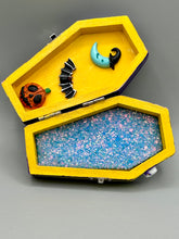 Load image into Gallery viewer, Coffin shaped box features a Day of the Dead kitty cat wearing a cute witchy hat while standing next to her witchy broom and a flying bat friend. The inside of the coffin is adorned with a witchy crescent moon, Jack-O-Lantern and a cute bat. This captivating coffin box makes an eye-catching, bewitching and whimsical Halloween-themed art piece that adds a one-of-a-kind Halloween touch to any home or office. L: 4 7/8"; W: 3"; H: 1 1/2"