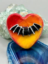 Load image into Gallery viewer, This hand-crafted art magnet is featuring a black bat with an ombre background of yellow, orange and bright red. This art clay magnet is the ideal home decor for Halloween enthusiasts. Perfect for adorning a witchy altar, goth, or spooky Halloween home decor. Halloween magnet art to add to your fridge, locker, cubicle or toolbox. This hand-crafted heart-shaped magnet features a black bat figurine with ombre colors of yellow, orange and bright red.