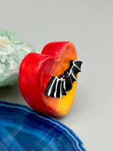 Load image into Gallery viewer, This hand-crafted art magnet is featuring a black bat with an ombre background of yellow, orange and bright red. This art clay magnet is the ideal home decor for Halloween enthusiasts. Perfect for adorning a witchy altar, goth, or spooky Halloween home decor. Halloween magnet art to add to your fridge, locker, cubicle or toolbox. This hand-crafted heart-shaped magnet features a black bat figurine with ombre colors of yellow, orange and bright red.