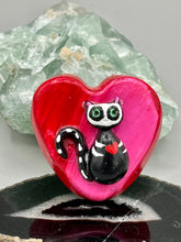 Load image into Gallery viewer, This hand-crafted art magnet is featuring a skeleton kitty cat, is the ideal home decor for cat lovers, Halloween, or Day Of The Dead enthusiasts. Perfect for adorning Day of the Dead ofrenda, a witchy altar, goth, or spooky Halloween home decor. Purrfectly cute and spooky Halloween magnet art to add to your fridge, locker, cubicle or toolbox. This hand-crafted heart-shaped magnet features a figurine of a black cat with ombre pink and red heart. 