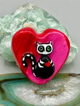 Load image into Gallery viewer, This hand-crafted art magnet is featuring a skeleton kitty cat, is the ideal home decor for cat lovers, Halloween, or Day Of The Dead enthusiasts. Perfect for adorning Day of the Dead ofrenda, a witchy altar, goth, or spooky Halloween home decor. Purrfectly cute and spooky Halloween magnet art to add to your fridge, locker, cubicle or toolbox. This hand-crafted heart-shaped magnet features a figurine of a black cat with ombre pink and red heart. 