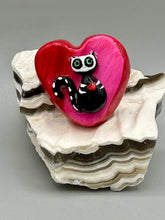 Load image into Gallery viewer, This hand-crafted art magnet is featuring a skeleton kitty cat, is the ideal home decor for cat lovers, Halloween, or Day Of The Dead enthusiasts. Perfect for adorning Day of the Dead ofrenda, a witchy altar, goth, or spooky Halloween home decor. Purrfectly cute and spooky Halloween magnet art to add to your fridge, locker, cubicle or toolbox. This hand-crafted heart-shaped magnet features a figurine of a black cat with ombre pink and red heart. 