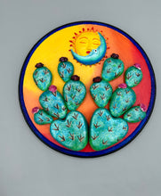Load image into Gallery viewer, Southwest inspired wall art comes in a circle-shaped wood frame with a sun and crescent moon motifs. Its warm sky hues, including yellow, orange and dark red, are further complemented by hand sculpted cacti plants with cool green-blue tones with light and dark pink flowers. Diameter 6 3/4"