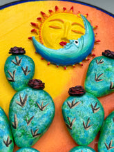 Load image into Gallery viewer, Southwest inspired wall art comes in a circle-shaped wood frame with a sun and crescent moon motifs. Its warm sky hues, including yellow, orange and dark red, are further complemented by hand sculpted cacti plants with cool green-blue tones with light and dark pink flowers. Diameter 6 3/4"