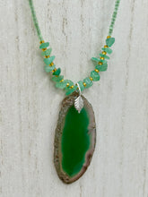 Load image into Gallery viewer, This Dark Green Agate Geode Sliced Stone Chip Necklace is a statement piece for your jewelry collection. It features a bold dark green agate geode pendant surrounded by a green aventurine, gold tone and green glass beaded necklace. The silver leaf bail completes this chic, Boho-inspired necklace.  Measurements:   Necklace is 19” in length - pendant is 2 1/4” Height