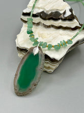 Load image into Gallery viewer, This Dark Green Agate Geode Sliced Stone Chip Necklace is a statement piece for your jewelry collection. It features a bold dark green agate geode pendant surrounded by a green aventurine, gold tone and green glass beaded necklace. The silver leaf bail completes this chic, Boho-inspired necklace.  Measurements:   Necklace is 19” in length - pendant is 2 1/4” Height