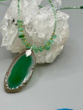 Load image into Gallery viewer, This Dark Green Agate Geode Sliced Stone Chip Necklace is a statement piece for your jewelry collection. It features a bold dark green agate geode pendant surrounded by a green aventurine, gold tone and green glass beaded necklace. The silver leaf bail completes this chic, Boho-inspired necklace.  Measurements:   Necklace is 19” in length - pendant is 2 1/4” Height