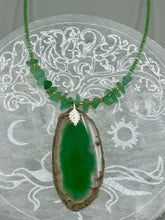 Load image into Gallery viewer, This Dark Green Agate Geode Sliced Stone Chip Necklace is a statement piece for your jewelry collection. It features a bold dark green agate geode pendant surrounded by a green aventurine, gold tone and green glass beaded necklace. The silver leaf bail completes this chic, Boho-inspired necklace.  Measurements:   Necklace is 19” in length - pendant is 2 1/4” Height