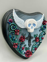 Load image into Gallery viewer, This Memento Mori Wall Art Decor is a one-of-a-kind art piece, skillfully crafted with a polymer clay skull and wings on a dark gray hear shape wood frame, decoratively woven with dark red roses and vines. It's perfect for adding an eye-catching touch to any wall and makes a unique, bold gift. W 6 1/2" x H 6 3/4"x D1 1/2"