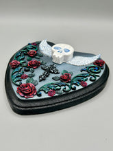 Load image into Gallery viewer, This Memento Mori Wall Art Decor is a one-of-a-kind art piece, skillfully crafted with a polymer clay skull and wings on a dark gray hear shape wood frame, decoratively woven with dark red roses and vines. It's perfect for adding an eye-catching touch to any wall and makes a unique, bold gift. W 6 1/2" x H 6 3/4"x D1 1/2"