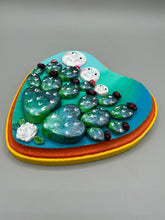 Load image into Gallery viewer, This handcrafted polymer clay wall art features a heart-shaped wood frame complimented with three smiling moon motifs.  Each moon symbolizing each of the realms of heavens, earth, and underworld. The complimentary color palette consists of cool sky hues, from a bright turquoise to a dark royal blue. The piece is further enhanced with hand sculpted cacti plants with blooming light and dark pink flowers.  The vibrant red and orange frame complements the cool-toned artwork.   H 7" x W 6 3/4” x D 1 1/4"