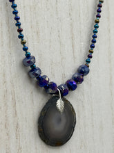 Load image into Gallery viewer, This Dark Gray-blue Agate Geode Sliced Stone Chip Necklace is a unique, eye-catching accessory to elevate your jewelry collection. The bold pendant features a striking gray-blue agate geode surrounded by eye-catching, shimmery dark-purple glass beads with beautiful iridescence that reflects hues of blue, pink, gold, and green. It's a perfect boho chic accent to update any look.   Measurements:   Necklace is 18” in length - pendant is 1 1/4” Height