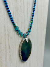 Load image into Gallery viewer, This Dark Blue Agate Geode Sliced Stone Chip Necklace is a luxurious addition to any jewelry collection. It features bold, eye-catching dark blue agate geode in an earthy outline, suspended on a unique glass beaded necklace that contains a mixture of blue and purple glass beads with a beautiful iridescence. This necklace is the perfect boho chic accent to take any look to the next level.   Measurements:    Necklace is 18” in length - pendant is 1 3/4” Height