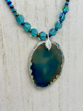 Load image into Gallery viewer, This Dark Blue Agate Geode Sliced Stone Chip Necklace is a luxurious addition to any jewelry collection. It features bold, eye-catching dark blue agate geode in an earthy outline, suspended on a unique glass beaded necklace that contains a mixture of blue and purple glass beads with a beautiful iridescence. This necklace is the perfect boho chic accent to take any look to the next level.   Measurements:    Necklace is 18” in length - pendant is 1 3/4” Height