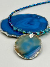 Load image into Gallery viewer, This Dark Blue Agate Geode Sliced Stone Chip Necklace is a luxurious addition to any jewelry collection. It features bold, eye-catching dark blue agate geode in an earthy outline, suspended on a unique glass beaded necklace that contains a mixture of blue and purple glass beads with a beautiful iridescence. This necklace is the perfect boho chic accent to take any look to the next level.   Measurements:    Necklace is 18” in length - pendant is 1 3/4” Height