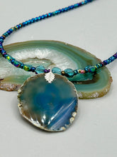Load image into Gallery viewer, This Dark Blue Agate Geode Sliced Stone Chip Necklace is a luxurious addition to any jewelry collection. It features bold, eye-catching dark blue agate geode in an earthy outline, suspended on a unique glass beaded necklace that contains a mixture of blue and purple glass beads with a beautiful iridescence. This necklace is the perfect boho chic accent to take any look to the next level.   Measurements:    Necklace is 18” in length - pendant is 1 3/4” Height