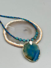Load image into Gallery viewer, This Dark Blue Agate Geode Sliced Stone Chip Necklace is a luxurious addition to any jewelry collection. It features bold, eye-catching dark blue agate geode in an earthy outline, suspended on a unique glass beaded necklace that contains a mixture of blue and purple glass beads with a beautiful iridescence. This necklace is the perfect boho chic accent to take any look to the next level.   Measurements:    Necklace is 18” in length - pendant is 1 3/4” Height