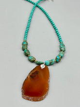 Load image into Gallery viewer, This unique and luxurious Amber Tone Agate Geode Sliced Stone Chip Necklace is a one-of-a-kind statement piece crafted from natural gemstones. The necklace features an amber-tone banded geode, suspended from a strand of blue and green turquoise and gold glass beads, and blue-green magnesite stone beads. This stylish boho-chic accessory is perfect for any casual or formal occasion. Measurements: Necklace is 18” in length - pendant is 2 1/2” Height