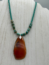Load image into Gallery viewer, This unique and luxurious Amber Tone Agate Geode Sliced Stone Chip Necklace is a one-of-a-kind statement piece crafted from natural gemstones. The necklace features an amber-tone banded geode, suspended from a strand of blue and green turquoise and gold glass beads, and blue-green magnesite stone beads. This stylish boho-chic accessory is perfect for any casual or formal occasion. Measurements: Necklace is 18” in length - pendant is 2 1/2” Height