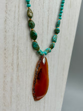 Load image into Gallery viewer, This unique and luxurious Amber Tone Agate Geode Sliced Stone Chip Necklace is a one-of-a-kind statement piece crafted from natural gemstones. The necklace features an amber-tone banded geode, suspended from a strand of blue and green turquoise and gold glass beads, and blue-green magnesite stone beads. This stylish boho-chic accessory is perfect for any casual or formal occasion. Measurements: Necklace is 18” in length - pendant is 2 1/2” Height