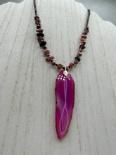 Load image into Gallery viewer, Unlock your inner goddess with this stunning Large Fuchsia Agate Geode Sliced Stone Chip Necklace. Featuring a vibrant fuchsia agate geode pendant surrounded by Rhodonite stone chips and gold and black glass beading, the silver leaf bail completes this chic and boho-inspired look. Make a bold statement with this bohemian-style gemstone necklace. Measurements: Necklace is 17 3/4” in length - pendant is 3” Height