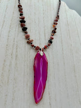 Load image into Gallery viewer, Unlock your inner goddess with this stunning Large Fuchsia Agate Geode Sliced Stone Chip Necklace. Featuring a vibrant fuchsia agate geode pendant surrounded by Rhodonite stone chips and gold and black glass beading, the silver leaf bail completes this chic and boho-inspired look. Make a bold statement with this bohemian-style gemstone necklace. Measurements: Necklace is 17 3/4” in length - pendant is 3” Height